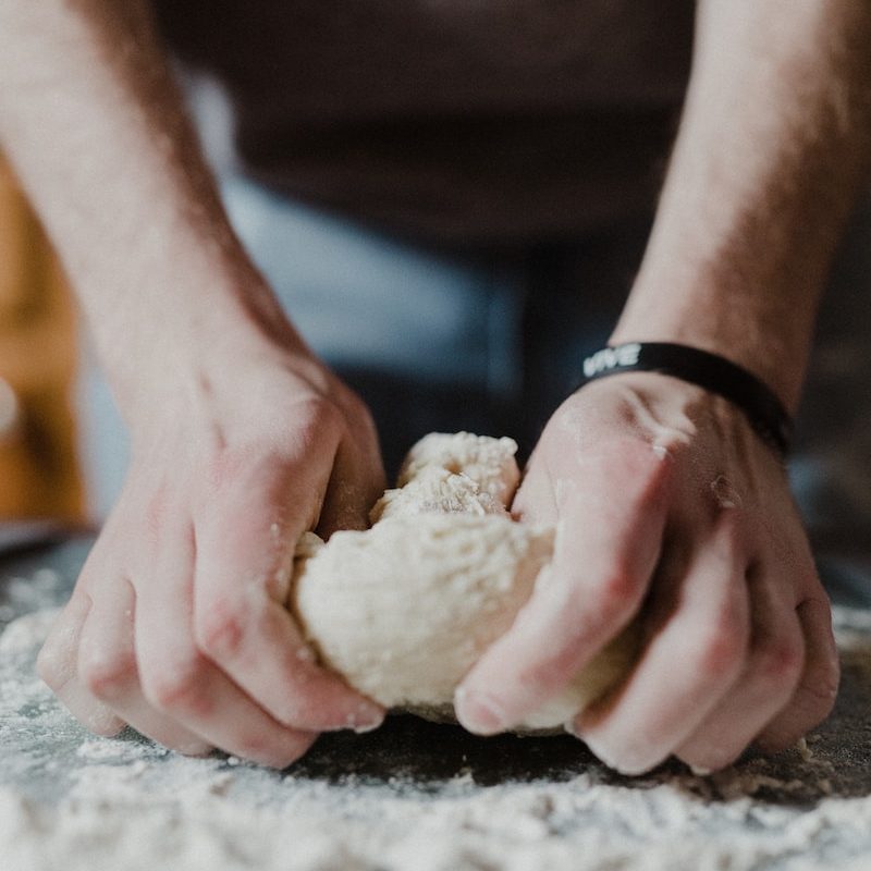 person holding white dough on brown wooden table